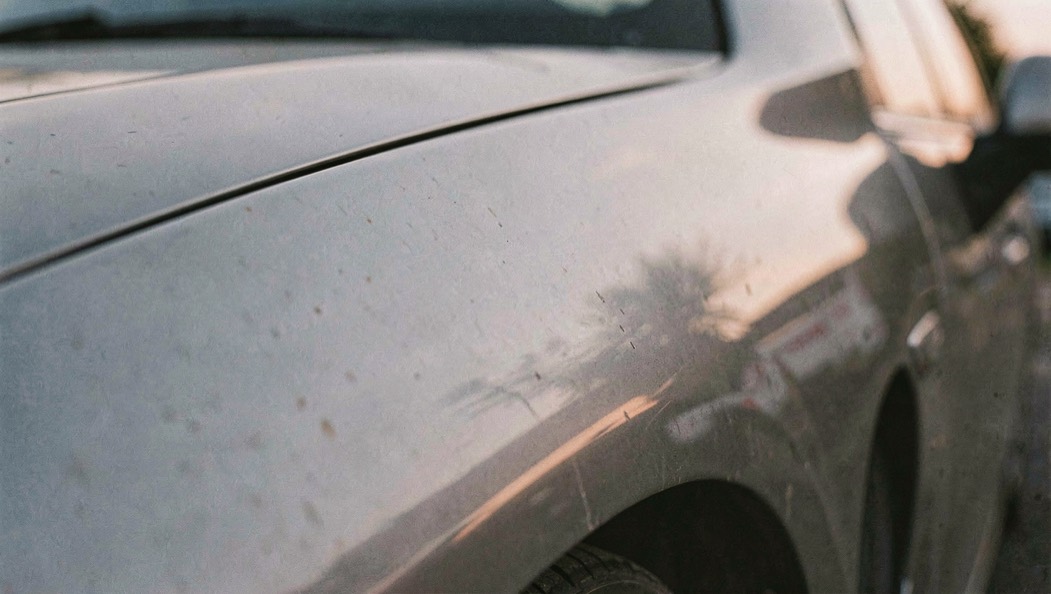 Gros plan sur l'aile d'une voiture garée en épi, reflets doux de la lumière du soir qui dessinent un léger creux dans la tôle