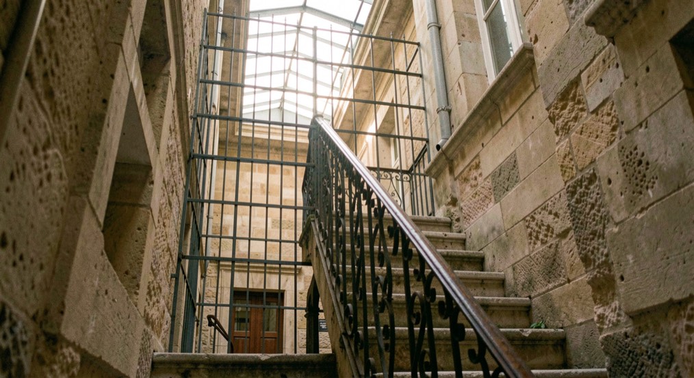 Cage d'escalier en pierre d'un immeuble ancien de Marseille, rampe en fer forgé et lumière douce tombant d'une verrière