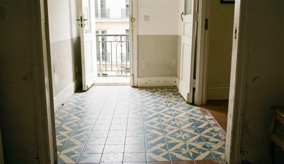 Sol de carreaux de ciment à motifs géométriques bleu et crème dans l'entrée lumineuse d'un appartement ancien de Marseille
